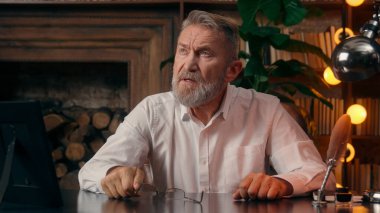 Kendinden emin, yaşlı, beyaz, olgun bir erkek kamera önünde el ele tutuşmuş ofis işadamı yakışıklı, yaşlı çalışan portresi liderinin içindeki iş adamına bakıyor.