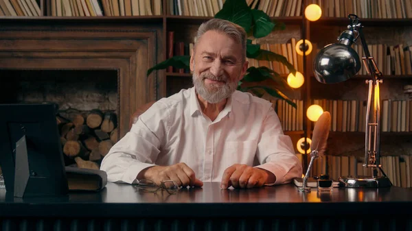 Kendinden emin, yaşlı, beyaz, olgun bir erkek kamera önünde el ele tutuşmuş ofis işadamı yakışıklı, yaşlı çalışan portresi liderinin içindeki iş adamına bakıyor.