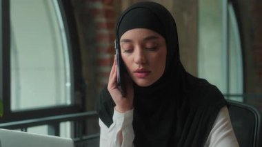 Ciddi Müslüman iş kadını Arap İslami iş kadını tesettürlü kadın yönetici girişimci danışman yönetici. Ofiste konuşan akıllı telefon konuşmasına cevap veriyor.
