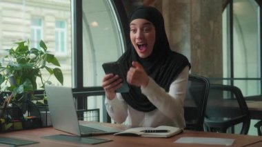 Arap Müslüman iş kadını tesettürde online bahsi kutluyor. Ofiste cep telefonuyla başarı kazandı. Neşeli bayan iş kadını akıllı telefon uygulaması ile sanal para kumarhanesi kazandı.