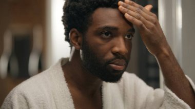 Aynaya bakan Afrikalı Amerikalı adam otel banyosunda gülümseyen sakallı adam sakal jölesi tıraş eden yumuşak cilt tıraşı sabah temizliği yapan erkek kozmetik ürünleri nemlendirici.