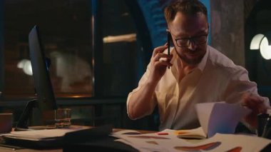 Kafkasyalı iş adamı, gece ofisindeki not defterine telefon arama notları yazarak meşgul iş adamı, erkek akıllı telefon görüşmelerini dizüstü bilgisayarla kontrol ederek vurguladı.