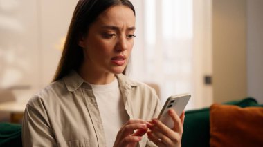 Kafkasyalı endişeli kullanıcı kadın elinde cep telefonuyla akıllı telefon hatunu tutmakta başarısız oldu. Hatalı uygulamalar internetteki modern teknoloji ağlarına mesaj yazıyor. Oturma odasında sorun var.