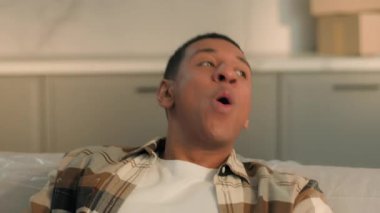 Gülümseyen mutlu Afro-Amerikan adam evinde dinleniyor tatmin oluyor erkek ev sahibi pozitif nefes alıyor rahat kanepenin yerini değiştiriyor yeni eve taşınıyor klimanın tadını çıkarıyor.