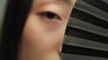 Asya 'lı kadın elinde pervaneyle kameraya bakıyor. Gizemli, güzel, güzel, çekici, Koreli, Çinli, bayan, göz kırpan sağlıklı bakışlı, kırpık bakışlı.