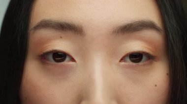 Kesik gözlü Koreli siyah kadın kameraya bakıyor. Kaşları yakın. Doğal kozmetik bakışlı Asyalı kadın.