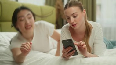 Kafkasyalı bir kadın cep telefonu kullanıyor. Asyalı bir kız bir araya geliyor. Yatakta uzanıyor, gülümsüyor, gülümsüyor, konuşuyor.