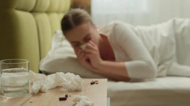 Beyaz kadın hapşırıyor, burun akıntısı var. Ev yatağında mendille hapşırıyor. Kadın hasta kadın gribi belirtileri var.