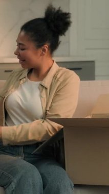 Mutlu Afro-Amerikalı kadın yeni yastıklarla kutuları açıyor kanepe alışverişinde online e-ticaret siparişleri alıyor kurye kız kurye kız paketleri açıyor taşınma günü taşınma günü kira dairesi için paketleri açıyor