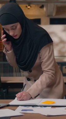 Müslüman, iş kadını, ofis işyerinde çoklu görev yapıyor. Telefon yazıları yazıyor. Dizüstü bilgisayar arıyor.