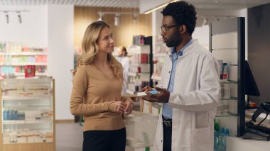 Eczacı doktor, eczane sağlık ürünlerindeki vitaminlerin satın alınmasına yardımcı olur. Afrikalı Amerikalı erkek, beyaz kadın eczane tıbbi konsültasyonu satın alır.