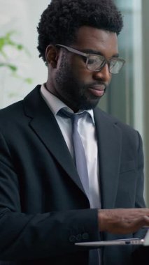 Pencereden dışarı bakan Afro-Amerikalı işadamı modern ofiste düşünceli erkek profesyonel iş adamı olarak çalışırken şirket stratejisi planlayıp gülümsüyor.