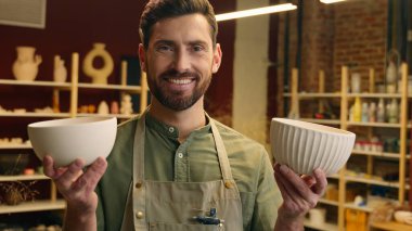 Mutlu gülümseyen beyaz erkek, erkek, küçük işletme sahibi, çömlek satıcısı, satıcı, iki porselen seramik kasesi gösteren, kapalı mekanlarda çömlek atölyesi satan, kameraya bakan adam.