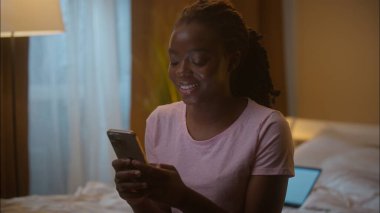 Mutlu gülümseyen Afro-Amerikan etnik kadın bayan bayan müşteri müşterisi cep telefonu kullanıyor akıllı telefon sohbet uygulaması yazarak ev yatak odasında iletişim kuruyor.