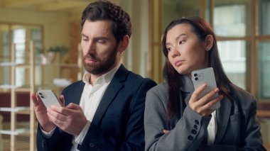 Çok ırklı Koreli iş kadını bakışları Kafkasyalı iş adamı cep telefonu ifadesi akıllı telefon karşılaştırması oyun başarısı kıskançlık cep telefonu cihaz ofis uygulaması online