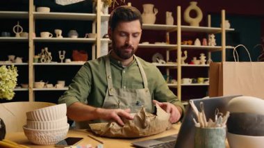 Dikkat et, beyaz adam, iş adamı, küçük işletme sahibi çömlekçi satıcı çanak çömlek sanat eseri seramik paketliyor, alışveriş çantası paketinde, ev içi atölye dizüstü bilgisayar dağıtıyor.