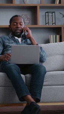 Afro-Amerikan aile babası evde çalışıyor çocuklar gürültü yapıyor babayı oynuyor bilgisayarla telefona odaklanmaya çalışıyor uzakta çalışıyor iki yaramaz çocuk kanepenin etrafında koşuyor