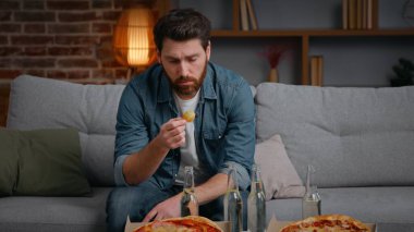 Beyaz, orta yaşlı, hayal kırıklığına uğramış bir adam pizza cipsi ile iptal edildi. Yalnız, yalnız, erkek adam kanepenin üzerinde yalnız, yalnız, kimsesiz doğum gününde yalnızlık karantinada acı çekiyor.