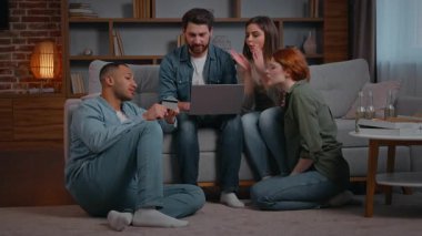 Çok ırklı dört arkadaş etnik çeşitlilik müşterileri dizüstü bilgisayarlı kredi kartı çevrimiçi hizmetleri ile yemek sipariş ediyor e-ticaret sitelerini kullanan gülümseyen insanlar oturma odasındaki partilerde kadın erkek web siteleri satın alıyorlar.