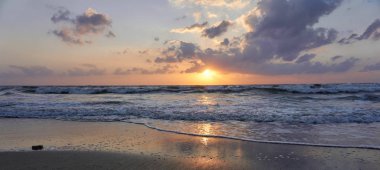 Netanya, İsrail plajda nefes kesen erken bahar günbatımı! Parlak turuncu güneş ufukta batıyor, köpüklü, dalgalı deniz üzerinde asılı güzel kabarık bulutlar.