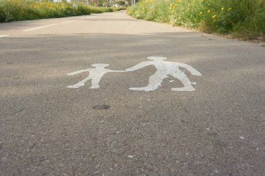 Yolda beyaz boya yaya tabelası. Yol kenarlarında görülebilen yeşil bitkiler. 