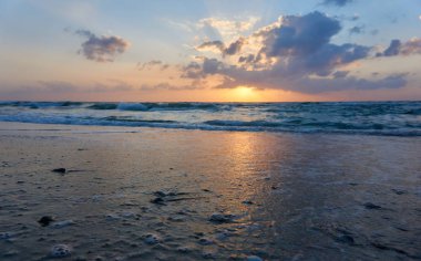 Erken ilkbaharda Netanya, İsrail plajda güzel gün batımı! Parlak turuncu güneş kabarık bulutların arkasında, köpüklü, dalgalı bir deniz üzerinde batıyor.