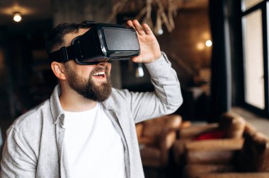 Sanal gerçeklik gözlükleri. Modern gülümseyen genç sakallı adam evde sanal gerçeklik gözlüğü takıyor. Sanal gerçeklikten hoşlanıyor.