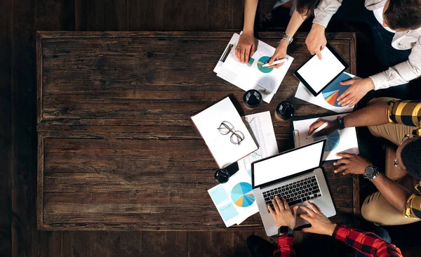 Top view of a desktop during a business meeting. A group of young multiethnic startupers are sitting at a desk in a modern office and discussing new ideas and technologies. Space for text