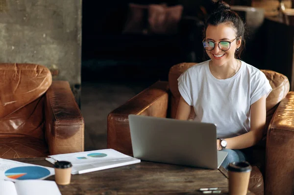 Online learning. Video call. Young cheerful girl with glasses learns distantly via video conference using a laptop while sitting at home