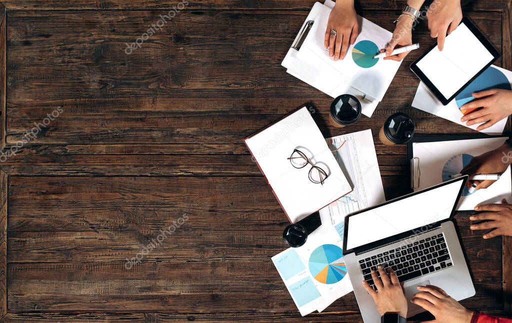 Top view of desktop with laptop tablet coffee documents and hands of colleagues. Business meeting in a modern office.Brainstorm of successful business partners.Colleagues develop new startups and ideas