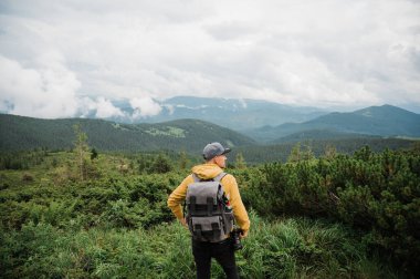 Sırt çantalı ve kameralı genç bir fotoğrafçı harika dağ manzarasından esinlenerek ayakta duruyor.