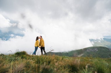 Sevgi dolu bir çift, el ele tutuşup dağın tepesinde güzel bir manzaranın arka planına karşı duruyor.