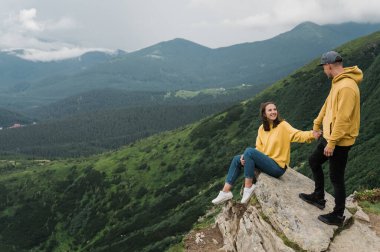 İlham verici bir manzara. Dağlarda aşk. Uçurumun kenarında birbirine aşık mutlu bir çift büyük bir kayanın arkasında inanılmaz bir dağ manzarasıyla birbirlerine bakıyorlar.