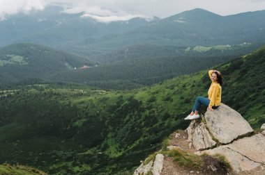 Genç bir kadın uçurumun kenarında oturur ve etrafındaki inanılmaz dağ manzarasının tadını çıkarır.