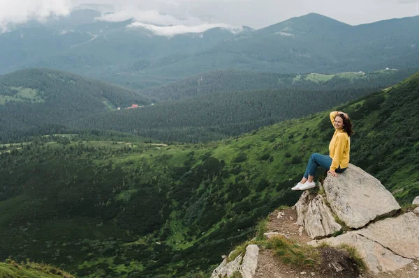 Genç bir kadın uçurumun kenarında oturur ve etrafındaki inanılmaz dağ manzarasının tadını çıkarır.