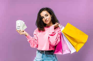 Alışveriş zamanı. Şaşırtıcı beyaz kadın izole edilmiş pembe arka planda duruyor kağıt alışveriş torbaları ve para tutuyor ve kameraya bakıyor.