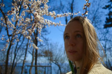 Yeşil gözlü ve sarı uzun saçlı genç, gülümseyen bir kız gözlerinin içine bakıyor. Kibar gözlerle sıcak gülümsüyor. Koyun derisi bir palto ve mavi bir gömlek giyiyor..