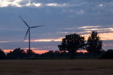 Yaz sıcacık akşamları, hasattan hemen sonra tarlaların üzerindeki manzara. Toplarda saman ve pembe bir gökyüzünün arka planında modern bir yel değirmeni.