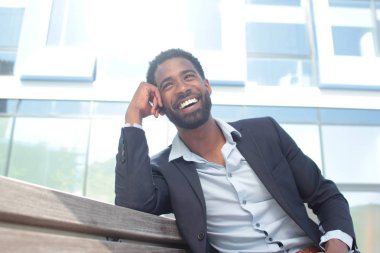 Bankta oturan ve gülümseyen siyah işadamı