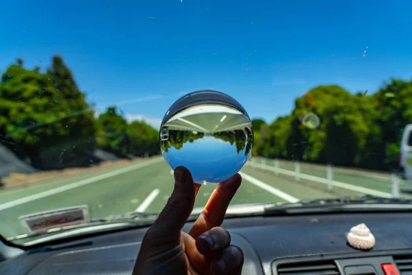 lens ball inside a car with a street in the background, crystal glas ball image with blue sky and a street