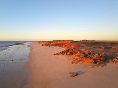 Okyanus, plaj, kırmızı kayalıklar, taşra manzarası ve fotokopi alanı olarak gün batımı mavi gökyüzü ile Broome, Batı Avustralya yakınlarındaki uzak sahil manzara havadan panoramik görünümü.