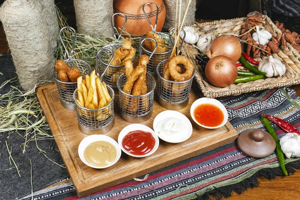 Oryantal tarzında şirket çeşitli aperatifler - soğan halkaları, şiş, patates kızartması, domates ve ekşi krema soslar bir dizi sosis