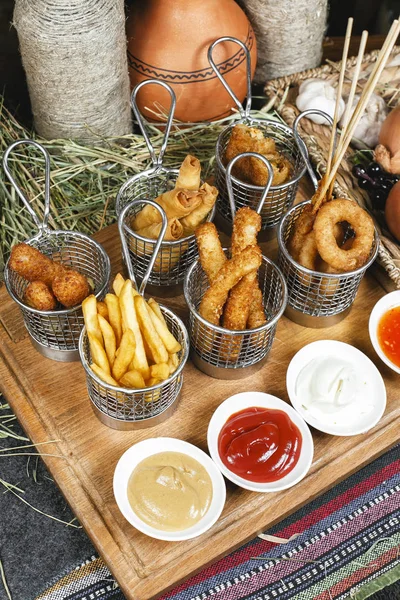 Oryantal tarzında şirket çeşitli aperatifler - soğan halkaları, şiş, patates kızartması, domates ve ekşi krema soslar bir dizi sosis