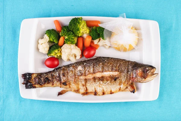 Mediterranean dish, European cuisine. whole fish baked in the oven, served with steamed vegetables - cauliflower, broccoli, carrots, cherry tomatoes and lemon