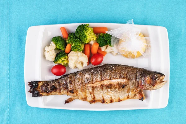 Mediterranean dish, European cuisine. whole fish baked in the oven, served with steamed vegetables - cauliflower, broccoli, carrots, cherry tomatoes and lemon