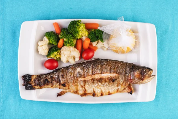 Mediterranean dish, European cuisine. whole fish baked in the oven, served with steamed vegetables - cauliflower, broccoli, carrots, cherry tomatoes and lemon