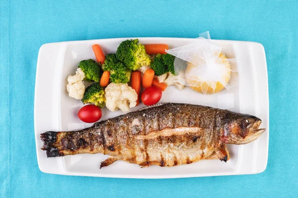 Mediterranean dish, European cuisine. whole fish baked in the oven, served with steamed vegetables - cauliflower, broccoli, carrots, cherry tomatoes and lemon