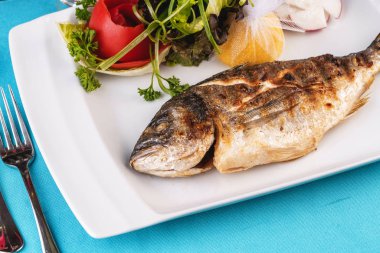 Akdeniz yemeği, Avrupa mutfağı. fırında pişmiş bütün balık, sebze, yeşillik, arugula, soğan halkaları, domates ve limon bir salata ile servis