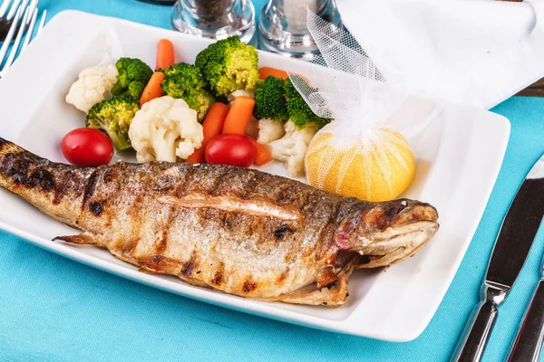 Mediterranean dish, European cuisine. Rainbow trout, grilled, served with vegetables - tomato, lettuce, radish, iceberg cabbage