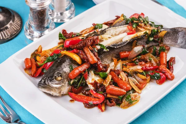 Seafood, Mediterranean cuisine, European dish. Whole fish baked with tomatoes with onion rings, red and green peppers, chili peppers, greens and vegetables. Caucasian national cuisine